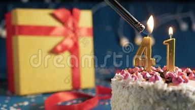 白色生日蛋糕编号41金蜡烛用打火机点燃，蓝色背景灯和礼品黄色盒子系好